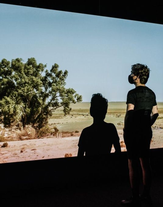 Instillation of moving image artwork Darling Darling. A man stand before a projected image of the Murray-Darling basin. 