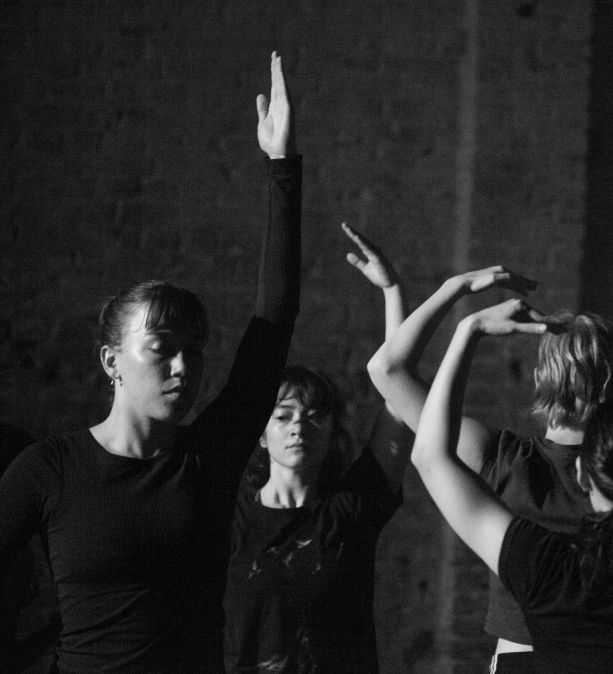 Black and white photo of dancers mid-performance with arms reaching up.