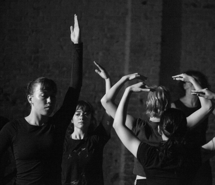 Black and white photo of dancers mid-performance with arms reaching up.