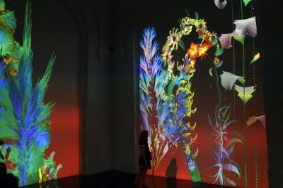 Woman standing dark room looking at a wall with flower projections.