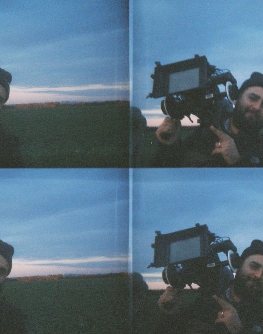 One image repeated four times in a grid. A man wearing a beanie holds a large camera over his shoulder. 