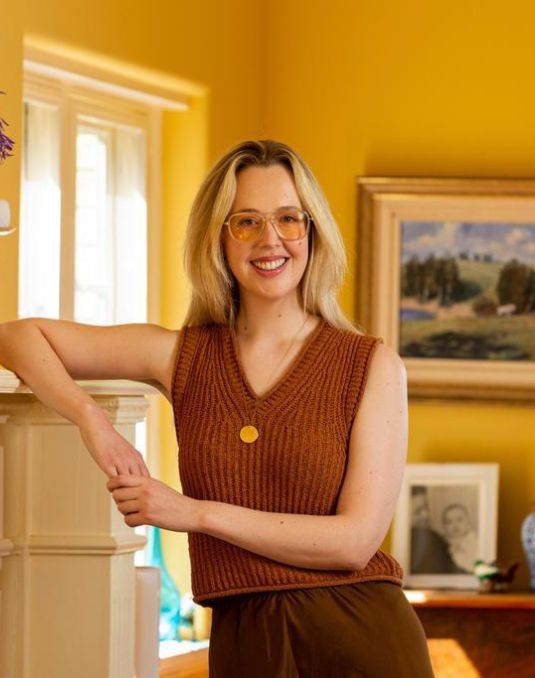 Blonde woman smiling and leaning against mantel. 