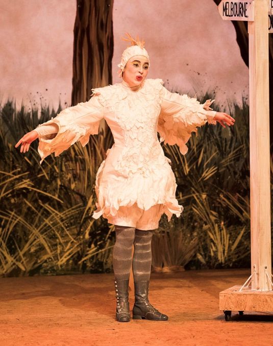 Woman on a stage dressed in a white bird costume and singing. 