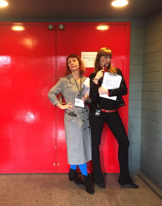 Two women pose in front of a red door. 