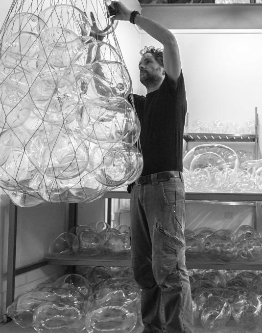 A man placing a blown glass sphere into a net suspended from the ceiling. 