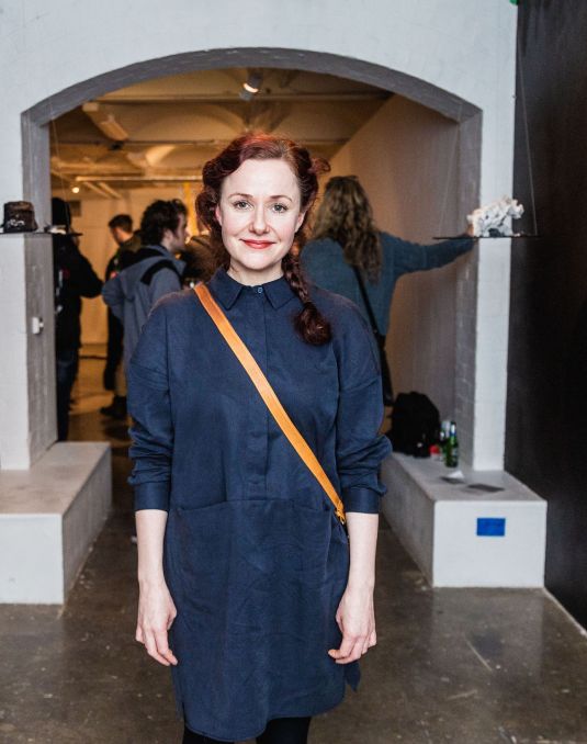 A woman standing in the middle of an archway. Ceramics are suspended on either side of her. 