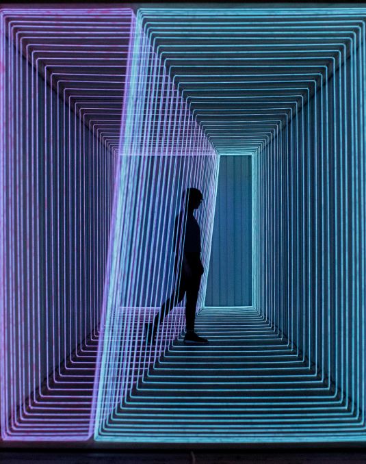 A person's silhouette walking through a glowing light installation. 