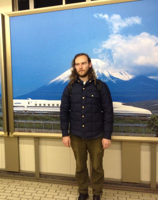 Man standing in front of a picture of a mountain. 