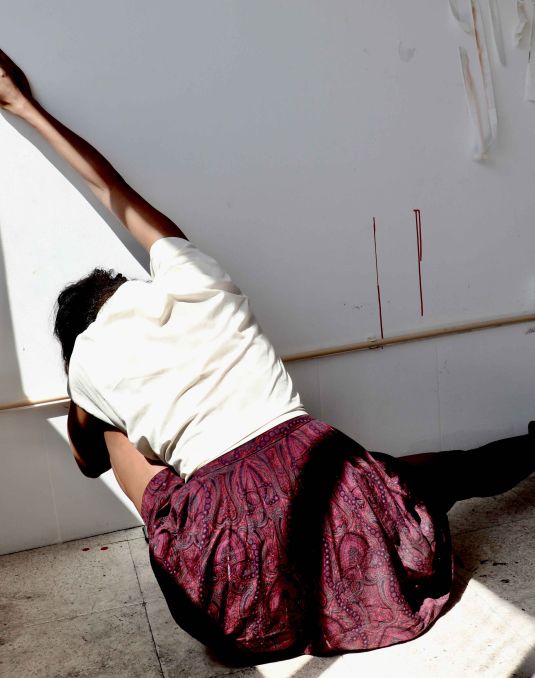 The back of a woman who is sitting down with her arm stretched against a wall. 