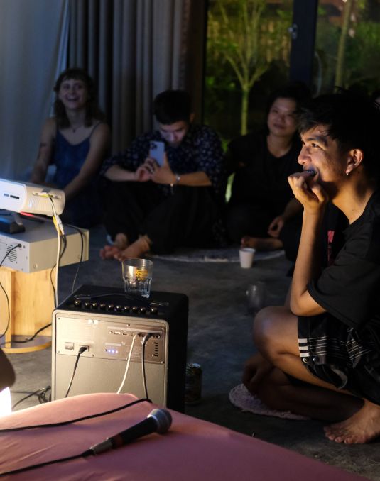 Group of people sitting on the floor in a dimly lit space watching a projection.