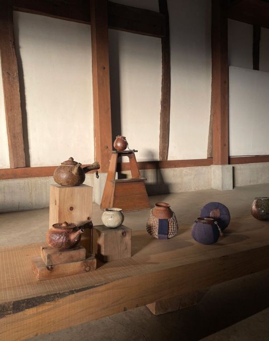 Several ceramic pieces sitting on a long wooden table and wooden stools.