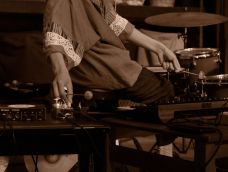 Sepia image of person on percussion set with hands altering the sound system.