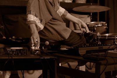 Sepia image of person on percussion set with hands altering the sound system.