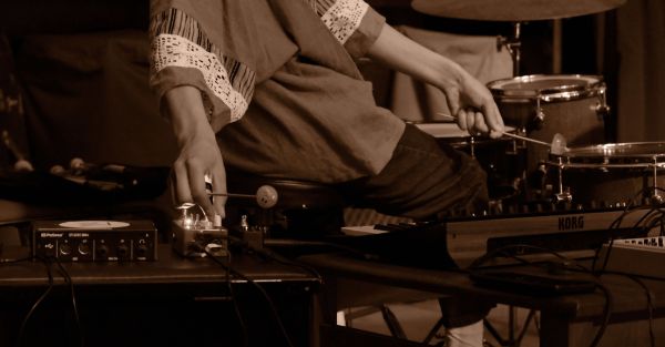 Sepia image of person on percussion set with hands altering the sound system.