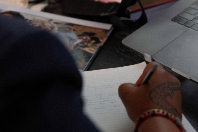 Artist's handwriting notes on desk with a camera and laptop perched nearby.