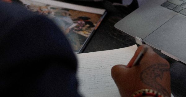 Artist's handwriting notes on desk with a camera and laptop perched nearby.