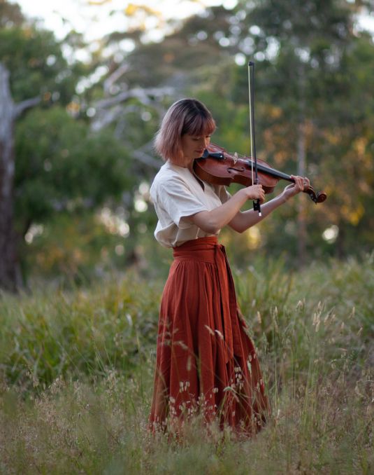 Woman in field playing string instrument.